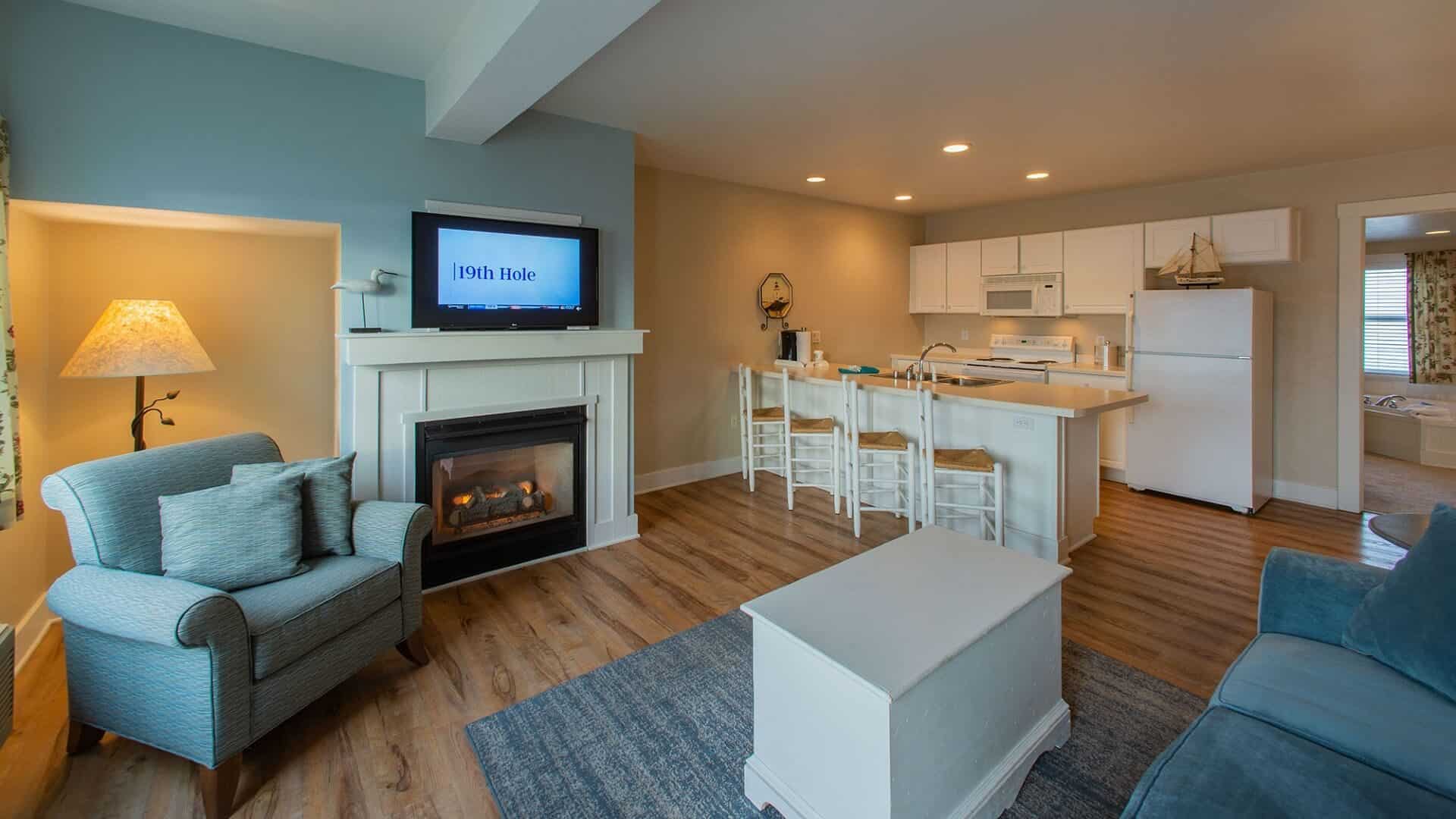 Suite with kitchenette, living room with blue couch and chair, fireplace, TV and doorway showing a jacuzzi tub