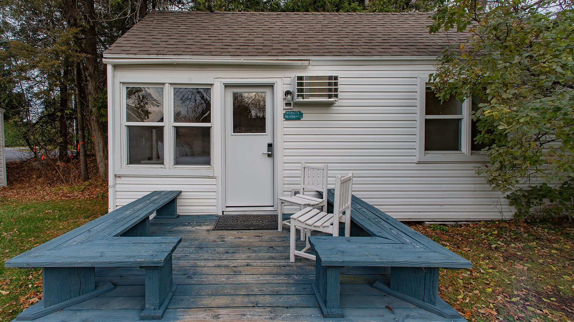 Small white cottage with front deck, bench seats and two white chairs