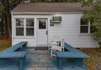 Small white cottage with front deck, bench seats and two white chairs