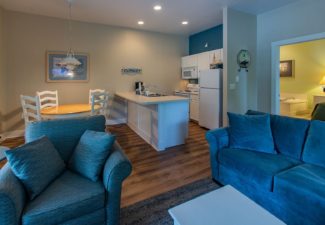 Hotel suite with kitchenette, hardwood floors, blue couch and chair and doorway into a bedroom with a jacuzzi tub