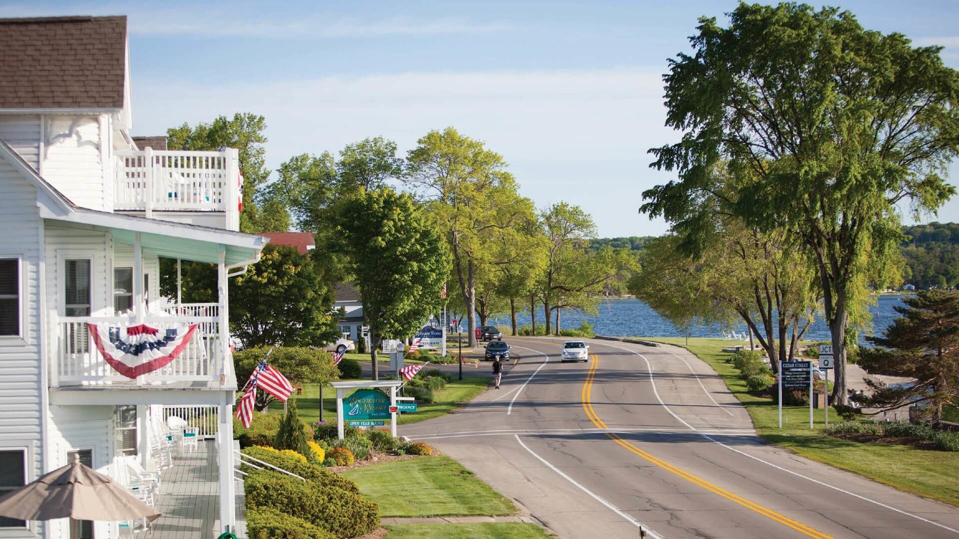 A winding road next to a large white three story home and large lake on the other side