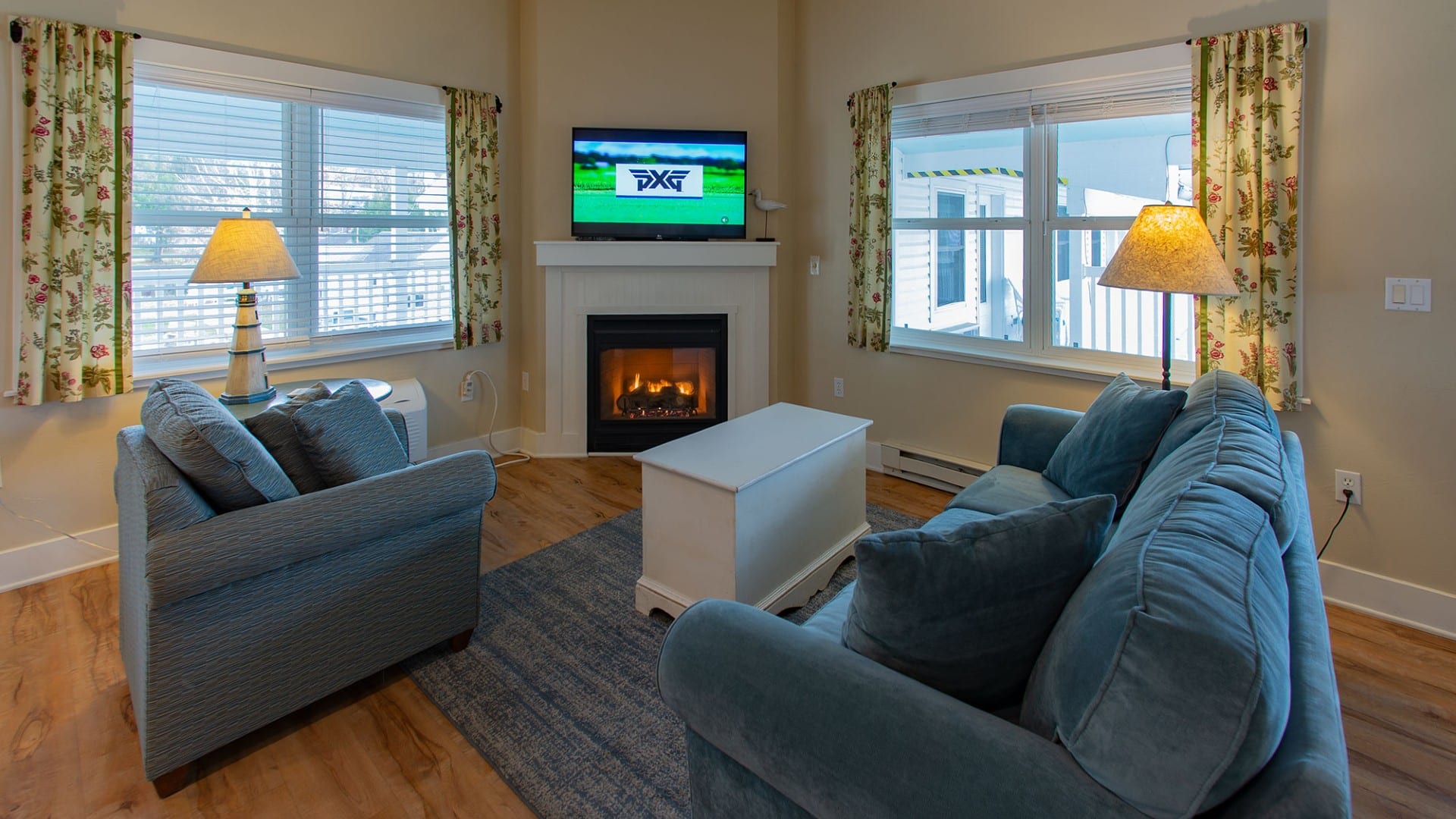 Living room of a hotel suite with plush couch and chair, gas fireplace and large windows with floral curtains