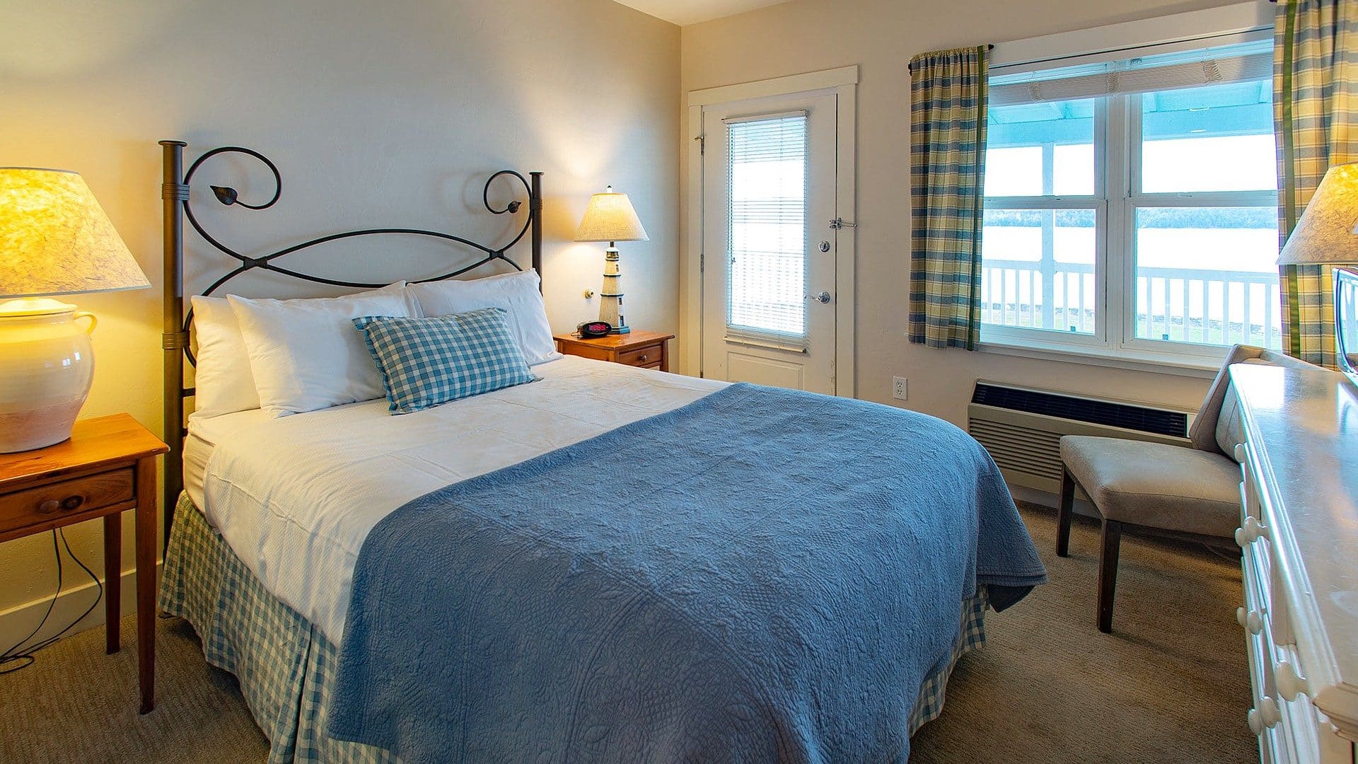 Bedroom with queen bed, side tables with lamps, sitting chair and picture window overlooking the water