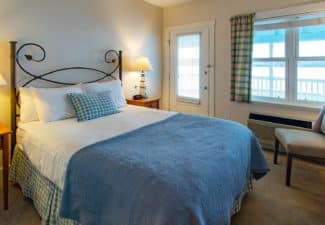 Bedroom with queen bed, side tables with lamps, sitting chair and picture window overlooking the water