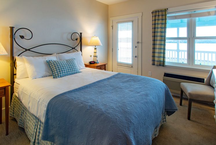 Bedroom with queen bed, side tables with lamps, sitting chair and picture window overlooking the water