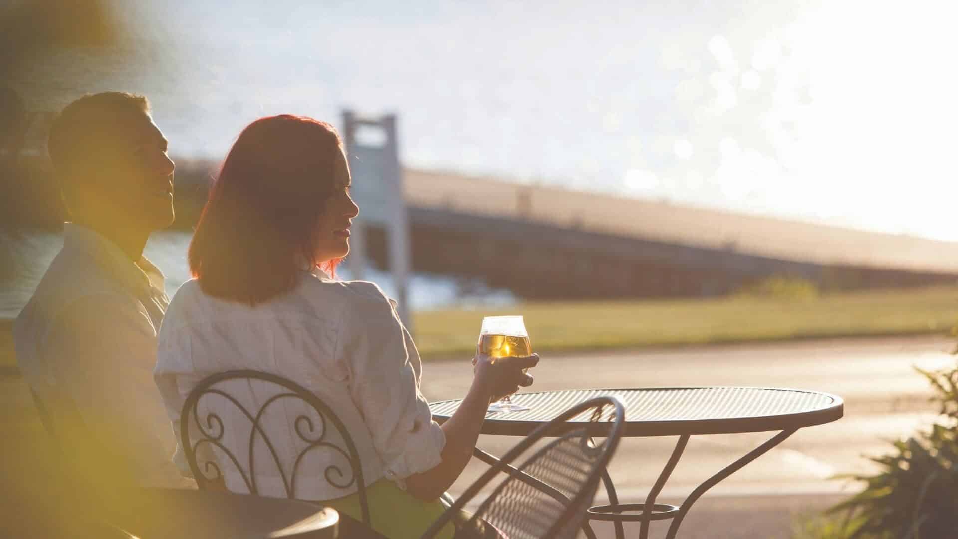 Man and woman sitting at an outdoor table with wine glass in hand with large dock in the background