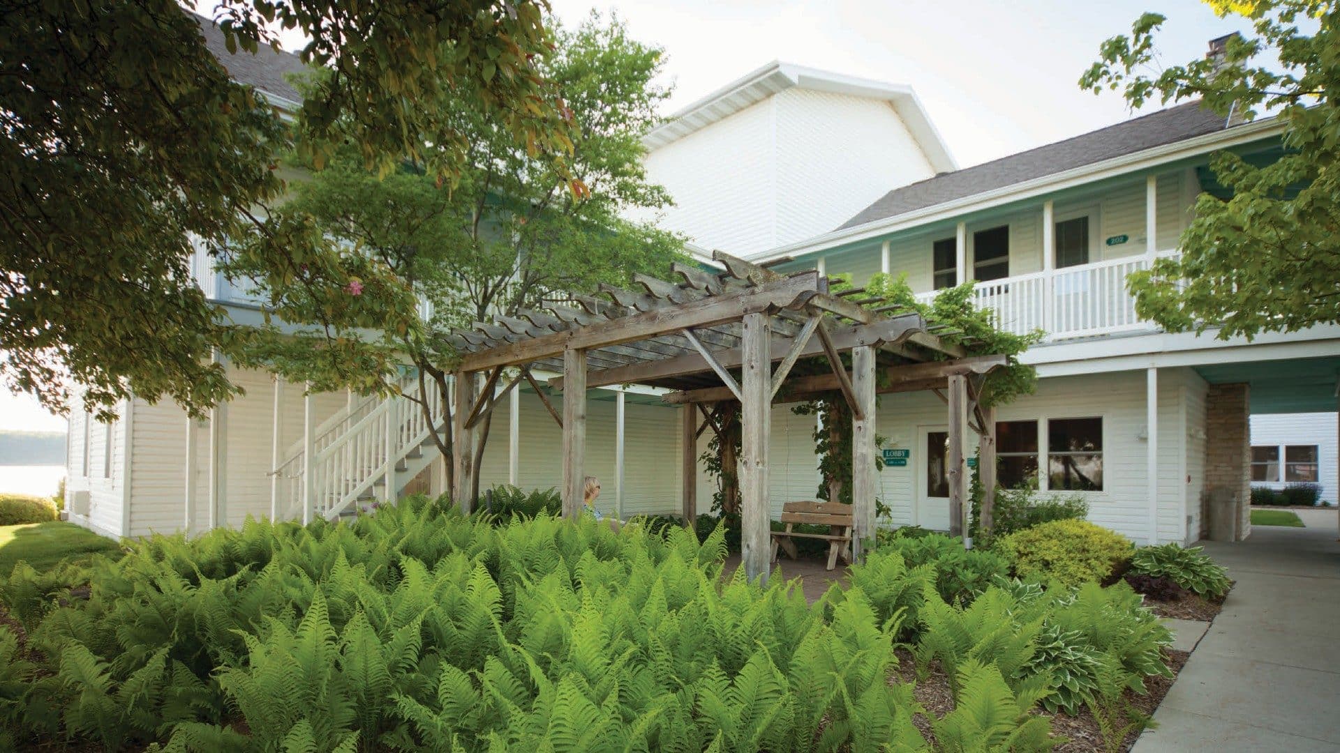 Exterior of two story hotel with wood arbor pergola among green ferns