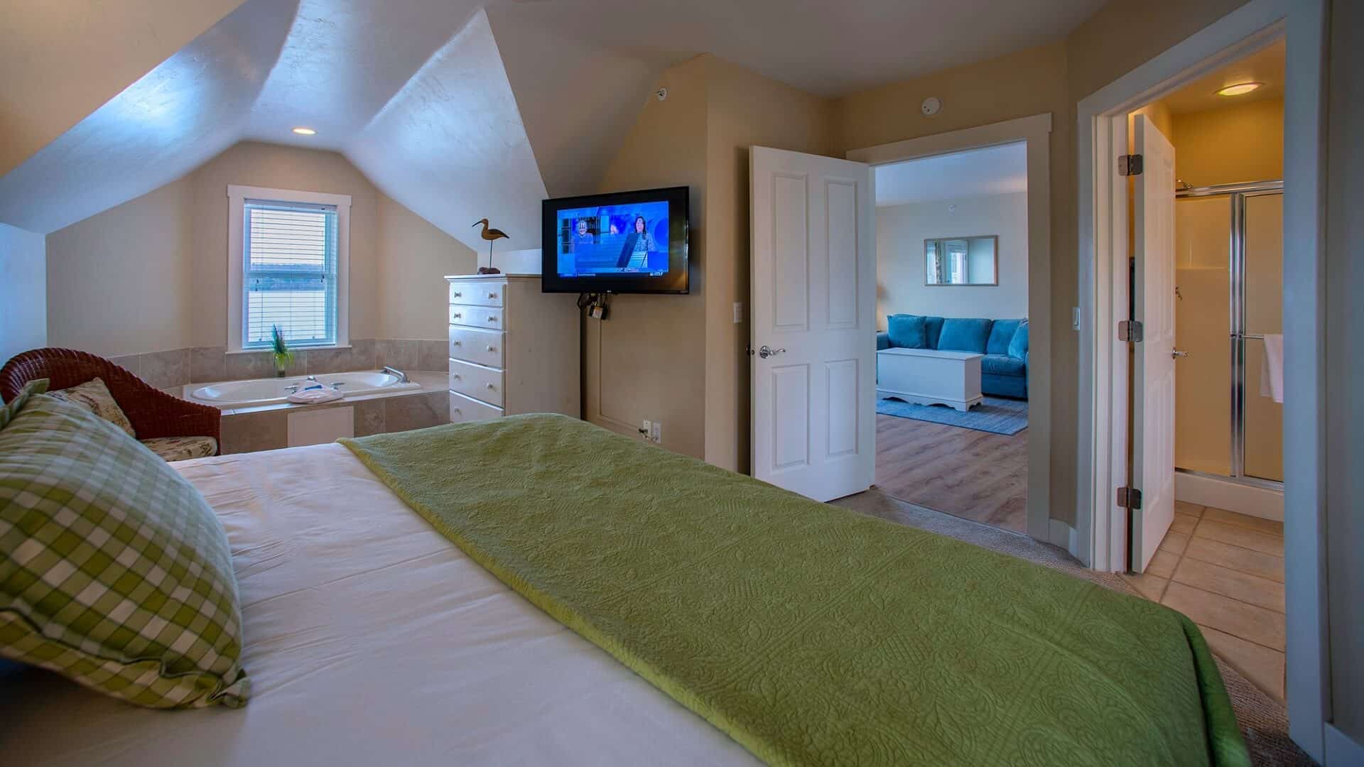 Spacious hotel suite with bedroom featuring king bed, jacuzzi tub, bathroom and doorway into a living area with a couch