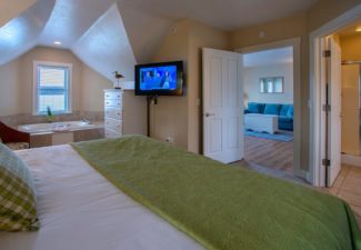 Spacious hotel suite with bedroom featuring king bed, jacuzzi tub, bathroom and doorway into a living area with a couch