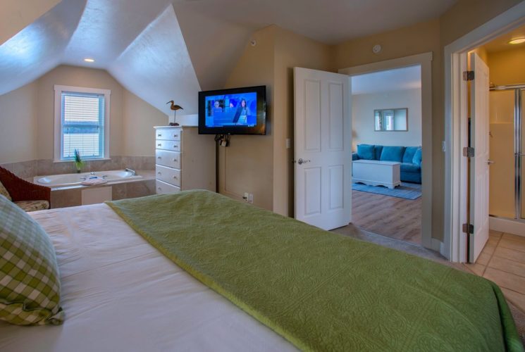 Spacious hotel suite with bedroom featuring king bed, jacuzzi tub, bathroom and doorway into a living area with a couch