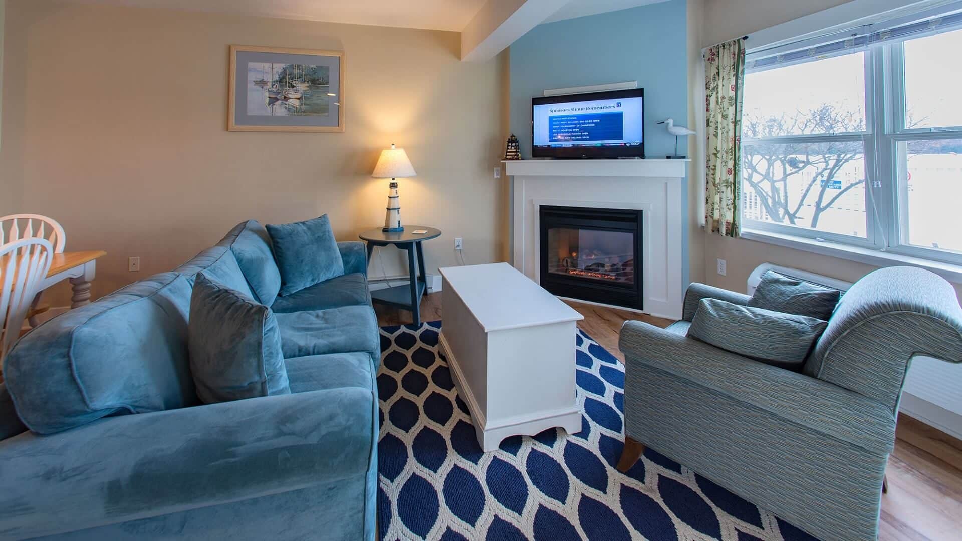 Living area of a suite with blue couch, chair, table, blue and white rug and large windows