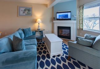 Living area of a suite with blue couch, chair, table, blue and white rug and large windows