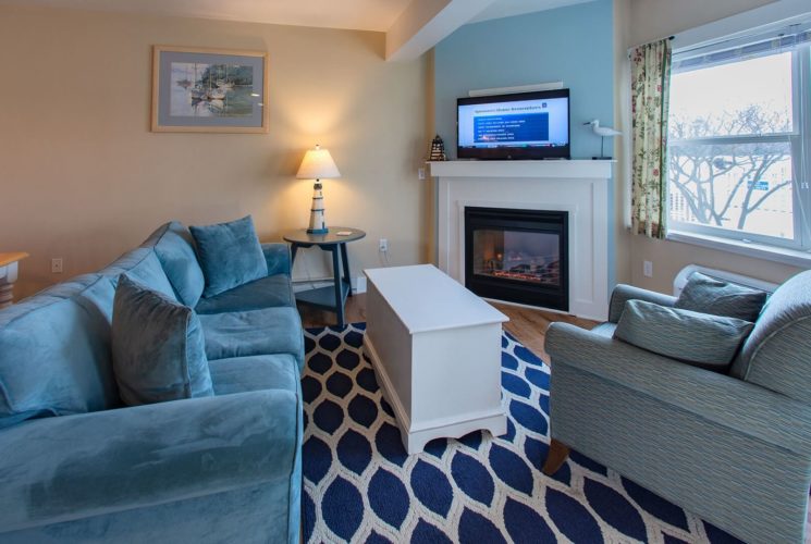 Living area of a suite with blue couch, chair, table, blue and white rug and large windows