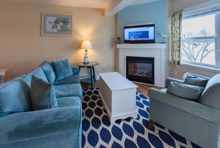 Living area of a suite with blue couch, chair, table, blue and white rug and large windows