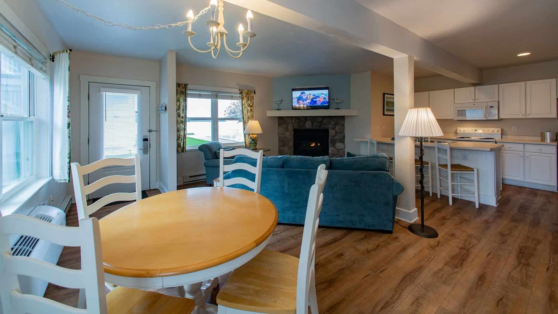 Hotel suite with kitchen, table and four chairs, and blue couch in front of a fireplace next to windows