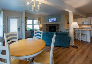 Hotel suite with kitchen, table and four chairs, and blue couch in front of a fireplace next to windows