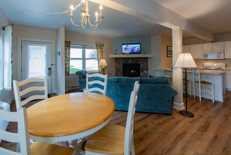 Hotel suite with kitchen, table and four chairs, and blue couch in front of a fireplace next to windows