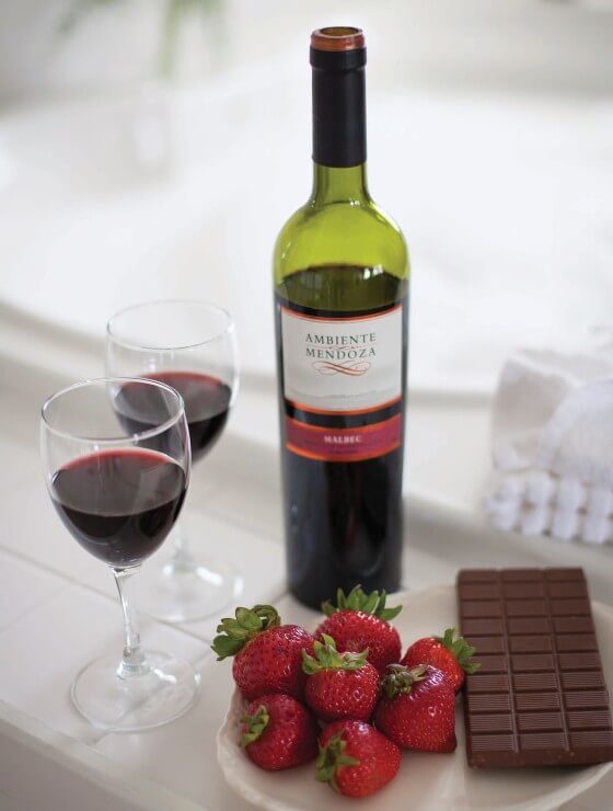 Bottle of red wine, two wine glasses and plate of strawberries and chocolate