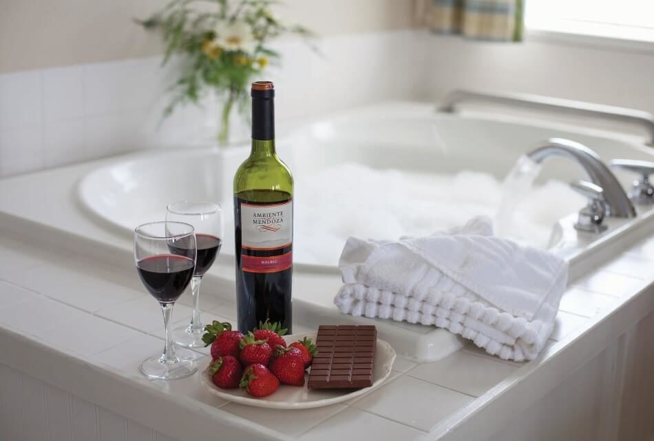 Jacuzzi tub filled with bubbly water with bottle of wine, two glasses and plate of chocolate and strawberries