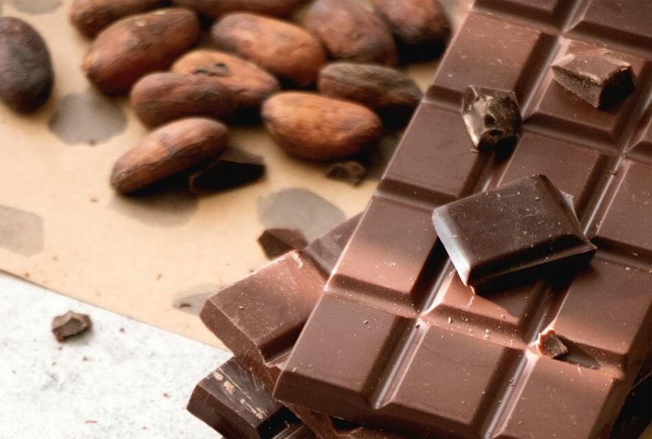 Chocolate bar with broken pieces next to some nuts on brown paper