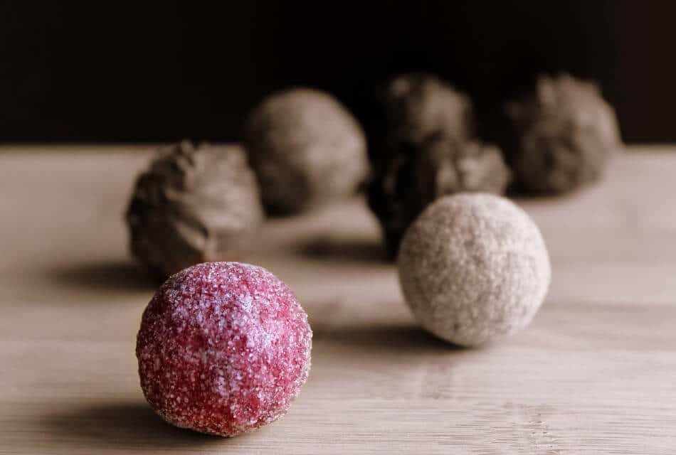 Seven brown and one red round truffle chocolates on a wood table