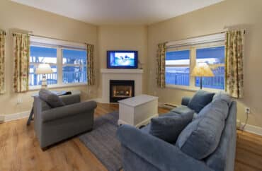 Hotel suite with full kitchen, bar stools, living room with couch and chair and bay window with floral curtains