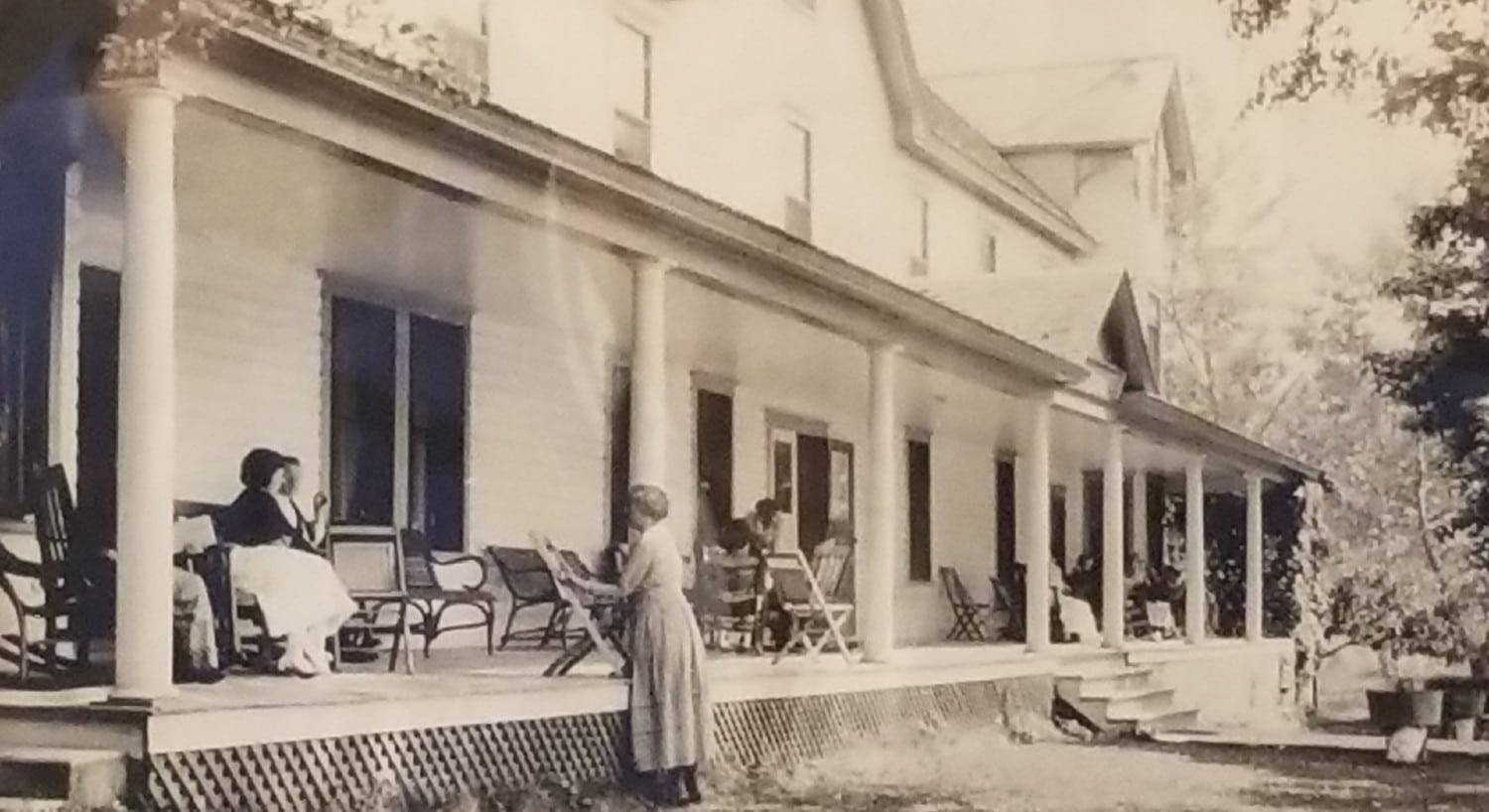A black and white historic photograph of a large hotel with a front porch full of patio chairs and three women talking