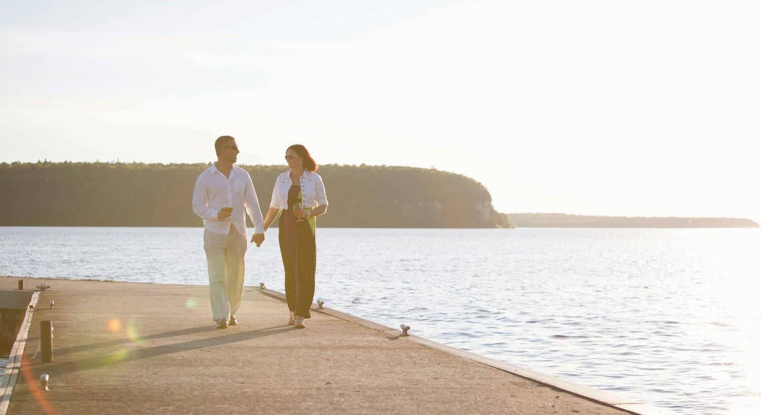 A man and woman holding hands walking down a paved walkway near a lake