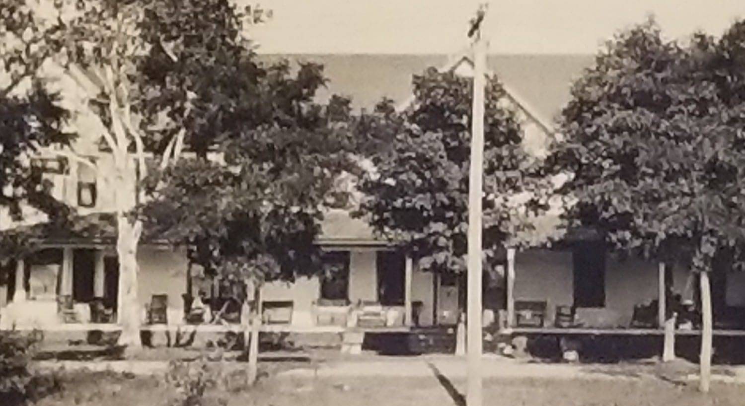 A black and white historic photograph of a hotel with large trees in front