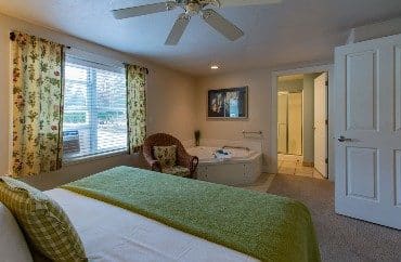 Bedroom with queen bed, large corner jacuzzi tub and picture window with floral curtains