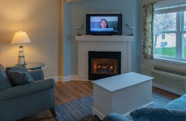 Cozy living room with couch, chair, table on a rug, gas fireplace with TV above and large picture window