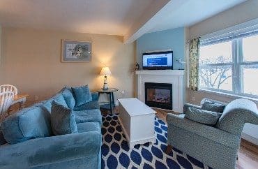 Living room with large blue couch and chair, patterned rug, coffee table and fireplace with TV on mantle