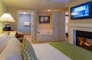 Large bedroom with king bed, gas fireplace with flat screen TV, jacuzzi tub and doorways into bathroom and living room