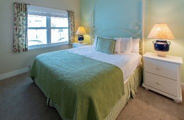 Bedroom with queen bed, white side tables with lamps and large picture window with floral curtains