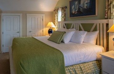 Bedroom with king bed, white and green linens, side tables with lamps and windows with floral curtains