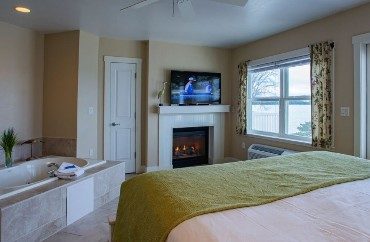 Bright bedroom with king bed, large soaker tub, fireplace with flat screen TV and large window with curtains