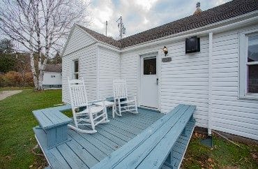 Small white cottage with blue front deck, bench seating and two white rocking chairs